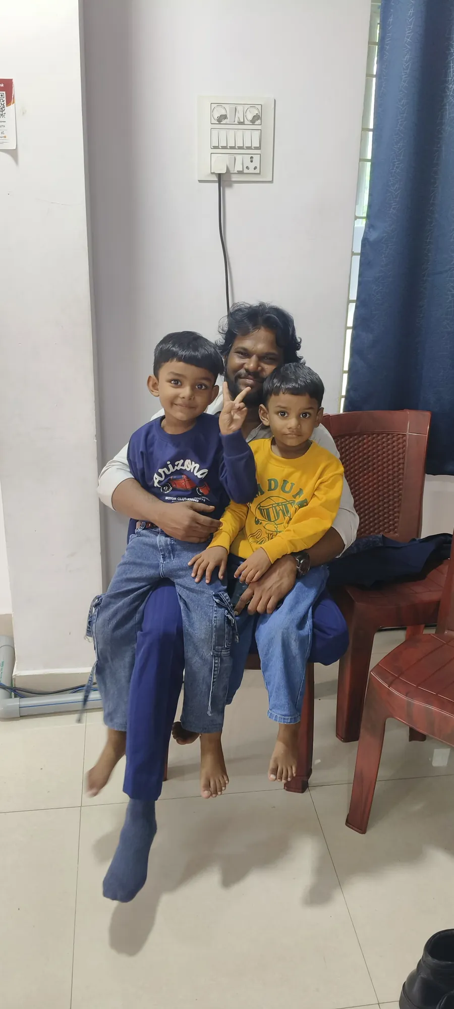 Anil and Abhishek sitting together on a man's lap, smiling